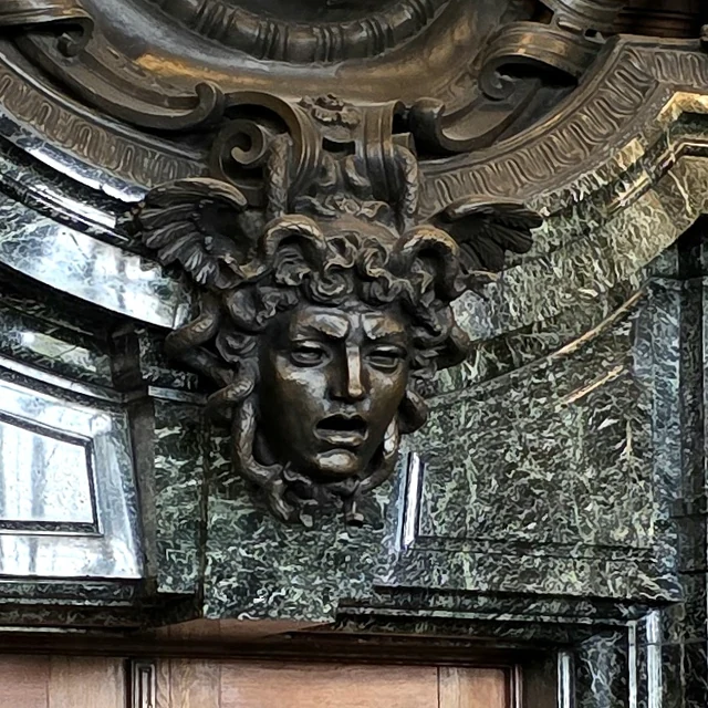 Fotografia da cabeça de Medusa em bronze sobre o portal de mármore verde da Sala 600, no Palácio da Justiça de Nuremberg.